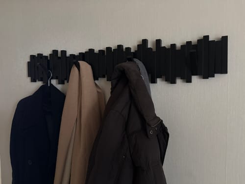 Recensent toont twee zwarte Umbra Sticks wandkapstokken naast elkaar aan een muur, met jassen eraan.