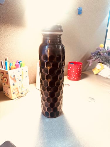 Customer's antique black diamond-cut copper water bottle sitting on a desk.