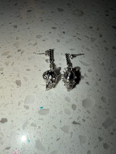 A customer's pair of detailed 6TH CIRCLE OF HELL EARRINGs in silver, laid flat on a countertop.