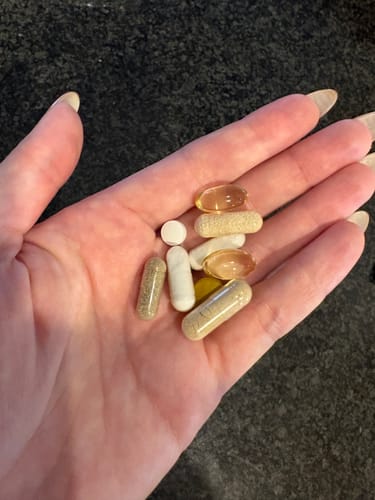 Customer holding a handful of daily supplements in their palm, including the Ashwagandha capsules.