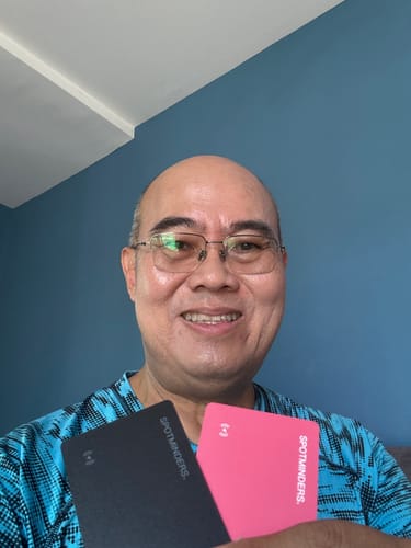 Reviewer smiling and holding two SPOTMINDERS Tracking Cards, one black and one pink.