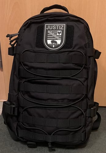 Rezensent zeigt den Justiz Black Ops Patch auf einem schwarzen Rucksack.