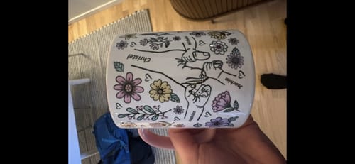 En kund visar upp sin Kärleksmugg med en personlig illustration av sammanlänkade händer, blommor och namn.