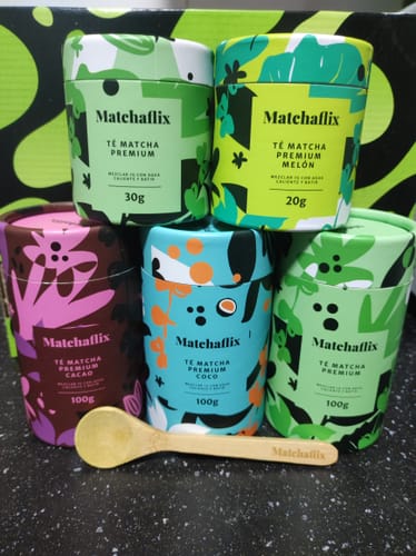 Un cliente muestra su colección de cinco botes de té matcha de varios sabores, apilados junto a una cuchara de madera.
