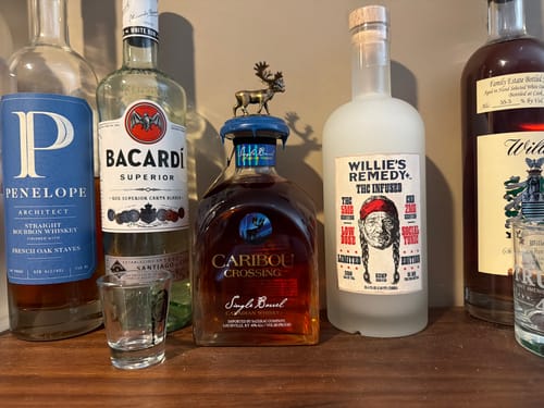 Customer's bottle of Caribou Crossing Single Barrel Canadian Whisky on a wooden shelf with other spirits.