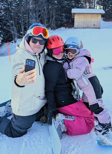 Reviewer in rose baggy snow pants posing for a family selfie on a snowy slope.