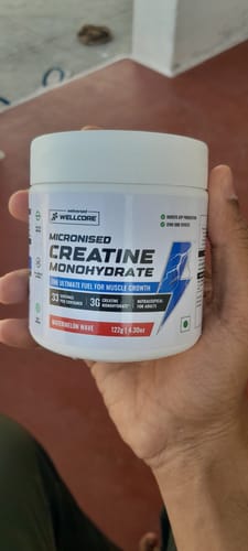 Reviewer holding a white tub of Wellcore Micronised Creatine Monohydrate in the Watermelon Wave flavor.