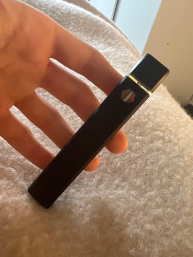 Customer holding the black, rectangular ROLLZ THCA Vape in their hand against a light-colored fabric background.