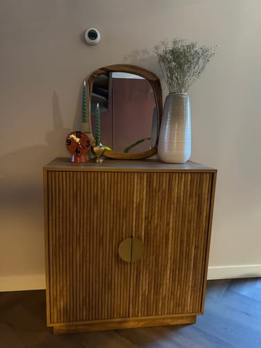 Beoordelaar's Exotisch dressoir met gegroefde deuren, gestyled met een spiegel, vaas en kaarsen in een woonruimte.