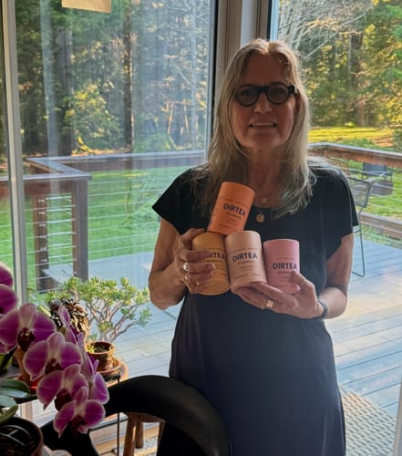 Reviewer holding four colorful containers from The DIRTEA Gummies Boxset in a bright room.
