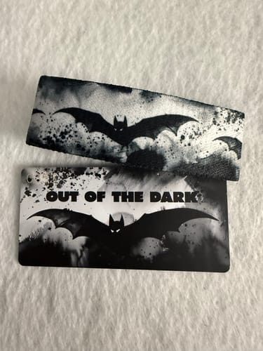 Reviewer's 'Out of the Dark' wrist strap and matching card, featuring a black-and-white bat design.