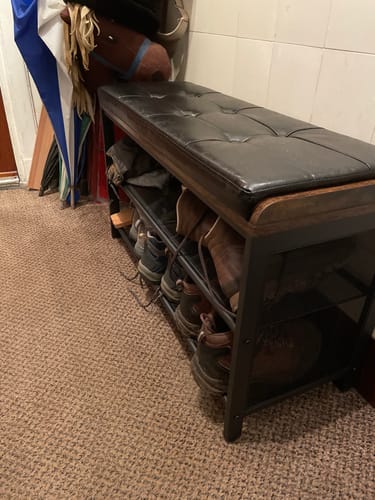 Klant toont het schoenenrek met bank in een hal, met planken vol schoenen onder de zwarte zitting.
