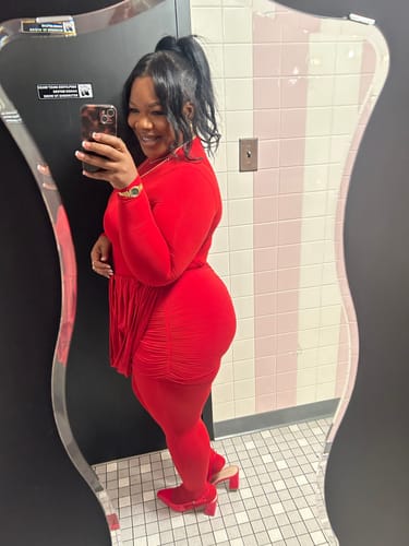 Reviewer in a mirror selfie wearing the bright red Naked Closed Toe Jumpsuit with a matching ruched skirt.