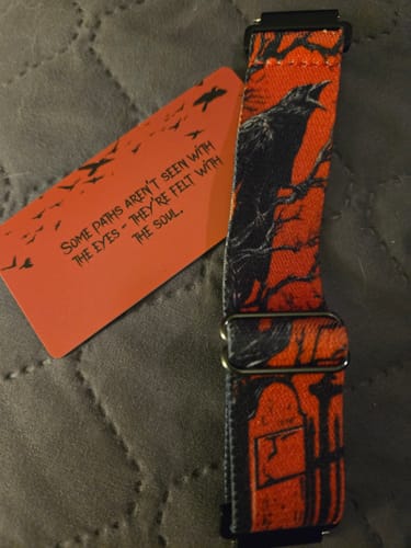 Customer's orange and black Dream Walker Watch Band with a raven design, shown flat on a quilted surface.