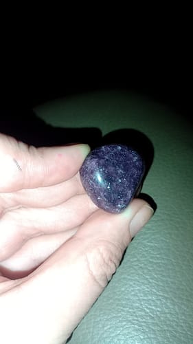 Customer holding a polished, dark purple Lepidolite crystal in their hand.