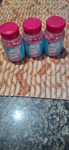 Cliente mostrando os três potes do suplemento vitamínico Happy Hair sobre uma mesa.