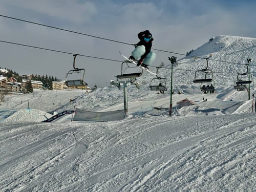 Reviewer mid-air on a snowboard, wearing the baggy ice blue snow pants on a snowy mountain.