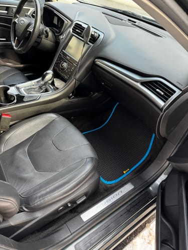 Zdjęcie klienta przedstawiające czarny dywanik samochodowy z niebieskim obszyciem, dopasowany do podłogi po stronie pasażera.