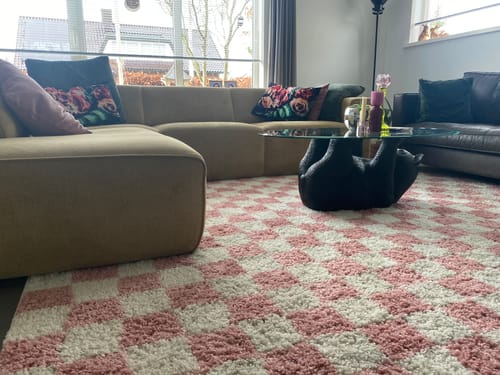 Klant toont het hoogpolige, geblokte vloerkleed in ivoor en roze in een woonkamer.