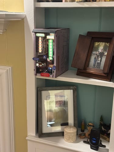 Reviewer's assembled Bangkok Yaowarat Book Nook Kit, lit up and displayed on a white bookshelf next to picture frames.