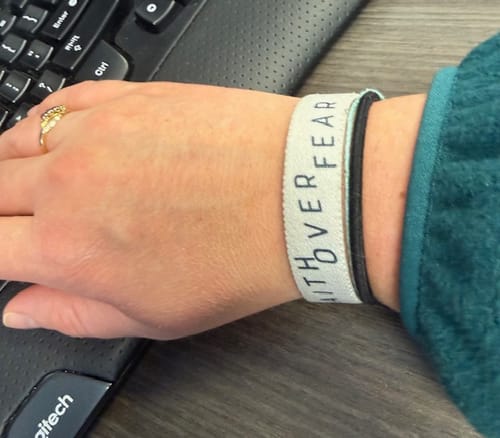 A reviewer wearing the white Faith Over Fear bracelet on their wrist next to a keyboard, showing the text.