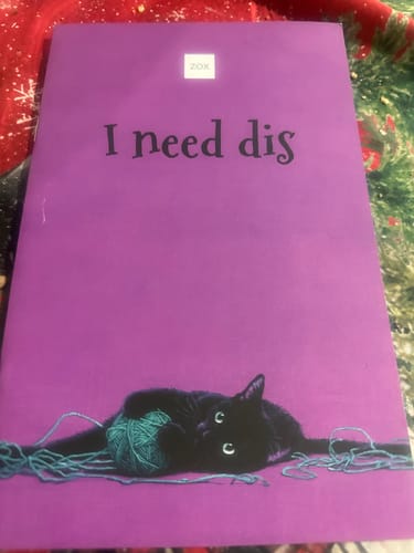 Customer's February 2026 Booklet with its purple cover showing a black cat tangled in teal yarn.