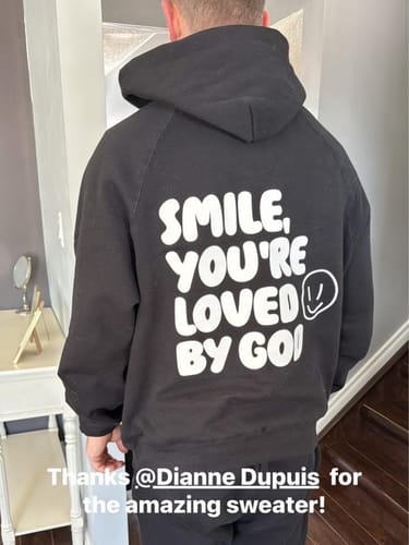 Customer from behind wearing the black Loved by God Oversized Hoodie, showing the 'Smile, You're Loved by God' back print.