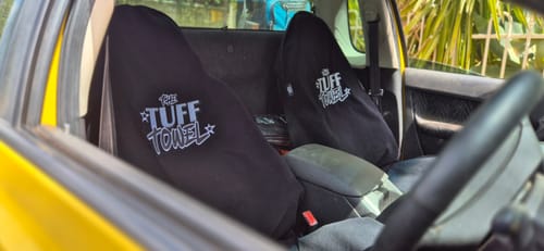 Customer's two black Tuff Towel seat covers installed on the front driver and passenger seats of a car, viewed from the side.