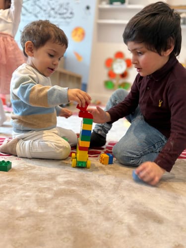 Customer image showing two children playing with colorful building blocks on a rug.