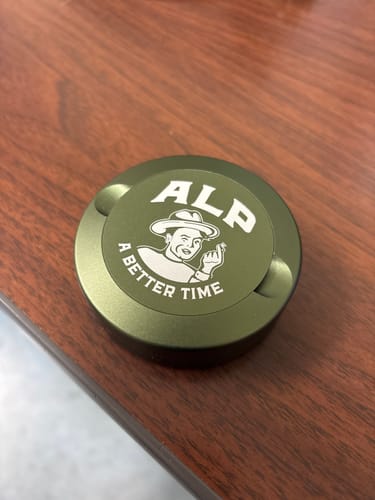 Customer's green tin of ALP Mountain Wintergreen Nicotine Pouches on a wooden desk.