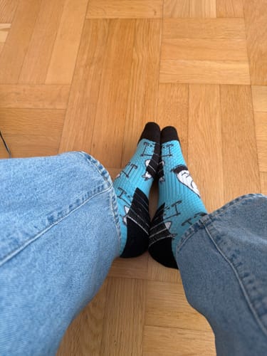 Kundens fötter i de ljusblå Mumin Stödstrumporna, sedda uppifrån på ett trägolv.