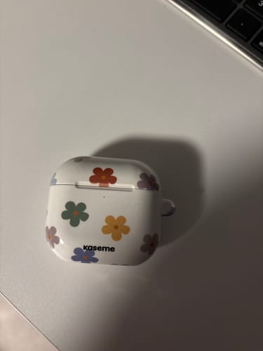 Customer's Woodstock Big AirPods Case with a colorful flower pattern shown on a white desk.