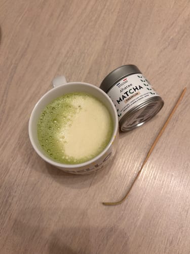 Un client montre sa tasse de thé matcha mousseux, avec la boîte de Thé Matcha Premium Bio à côté.