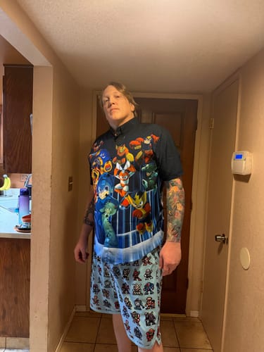 Reviewer wearing the black Mega Man "Powered Up" shirt with colorful character graphics indoors.