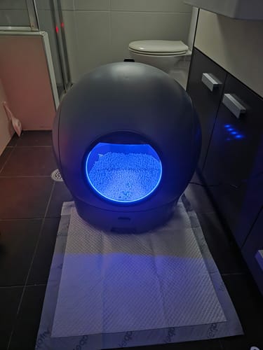 Customer's AutoClean Max litter box operating in a bathroom with its blue interior light on.