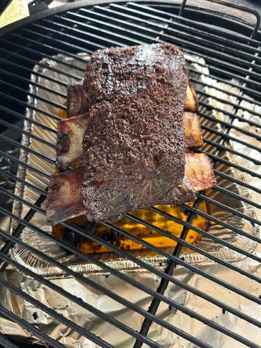 Customer's seasoned Bone-In Short Ribs with a dark crust, resting on a grill grate.