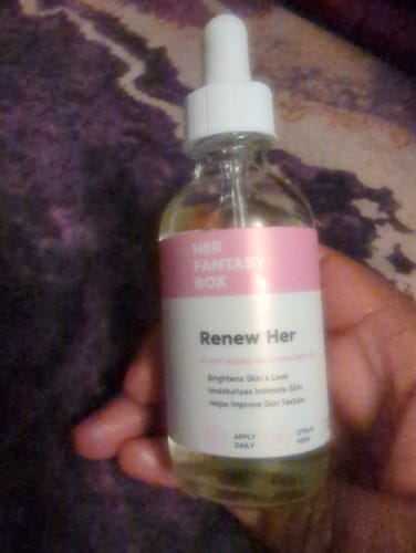 Customer holds a clear bottle of Her Fantasy Box Renew Her Yoni Oil with a white dropper and a pink label.