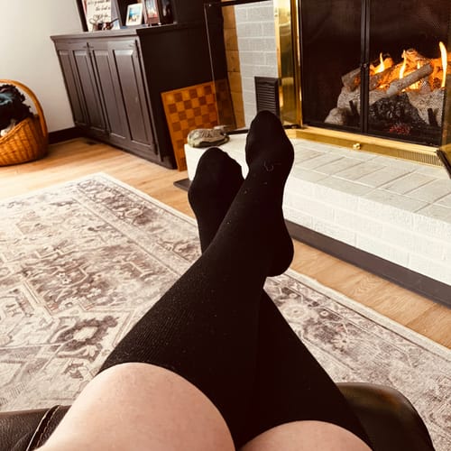 Reviewer wearing black Performance Eucalyptus Compression Socks with legs crossed while relaxing in a chair.