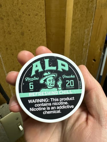 Customer holding a white, round can of ALP Refreshing Chill Nicotine Pouches, showing the front label.