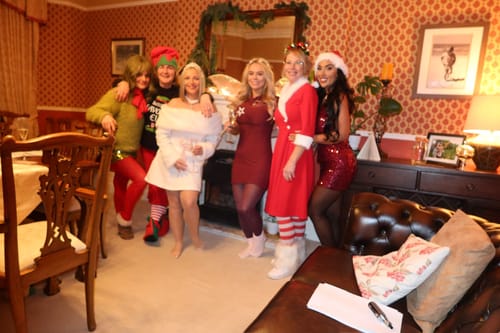 A group of reviewers in festive Christmas costumes posing for a photo while playing the murder mystery game.