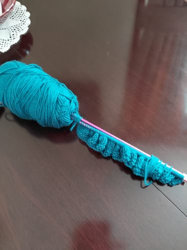 Customer's knitting project in progress with teal yarn from their Ladies Mystery Knitting Box on a table.
