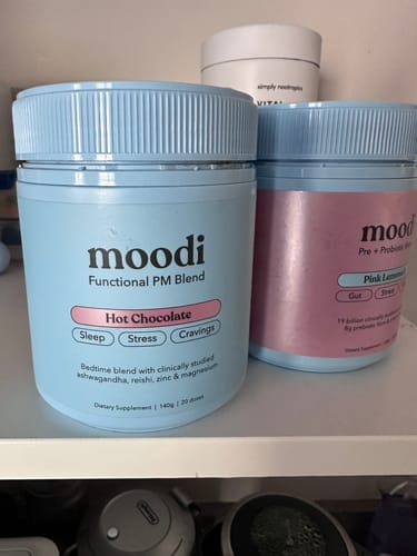 Customer's light blue tub of moodi Hot Chocolate PM Blend sitting on a shelf next to another product.
