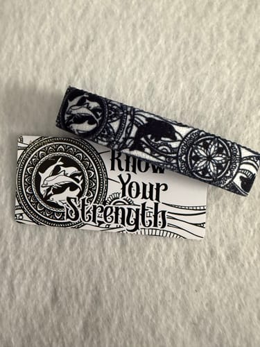 Reviewer's intricate Know Your Strength Bracelet with a black and white dolphin design, shown with its packaging.