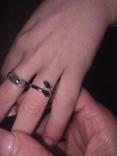 Customer's hand wearing a silver ring shaped like hugging arms, received as a Mystery Gift.