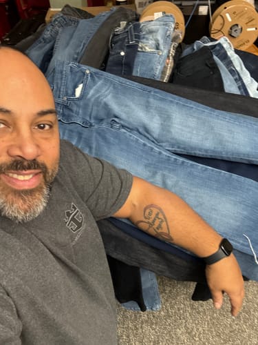 Reviewer smiling next to a large pile of assorted jeans from their wholesale order.