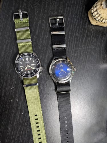 Customer's AlphaShark Army Green strap on a watch, placed next to another watch with a black strap.