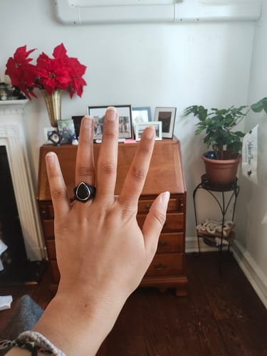 Reviewer's hand showing the black, oversized pear-shaped silicone ring with a metal frame.
