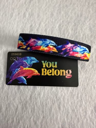 Customer's colorful You Belong Bracelet with a dolphin design, displayed next to its black backing card.