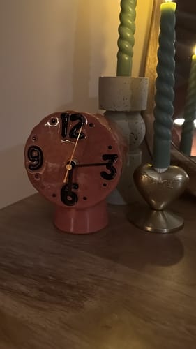 Close-up van de roze HKliving Retro Tafelklok van een klant, sfeervol verlicht op een houten meubel naast kaarsen.