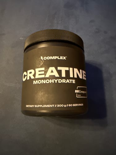 Customer's black tub of Complex Creatine Monohydrate supplement sitting on a dark surface.